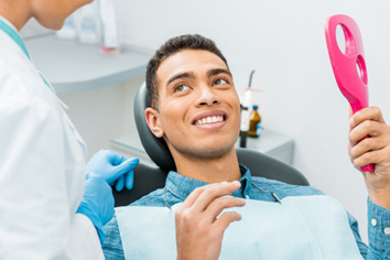 Man smiling at dentist while holding small mirror