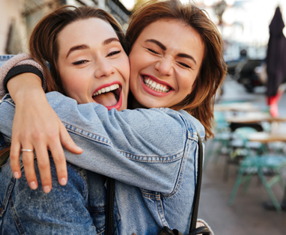 Woman in denim jacket hugging another woman