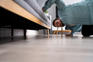 Man with glasses looking under a couch